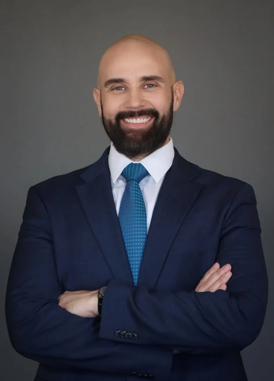 Attorney Ryan Alexander, solo studio portrait in a navy suit and blue tie, arms folded