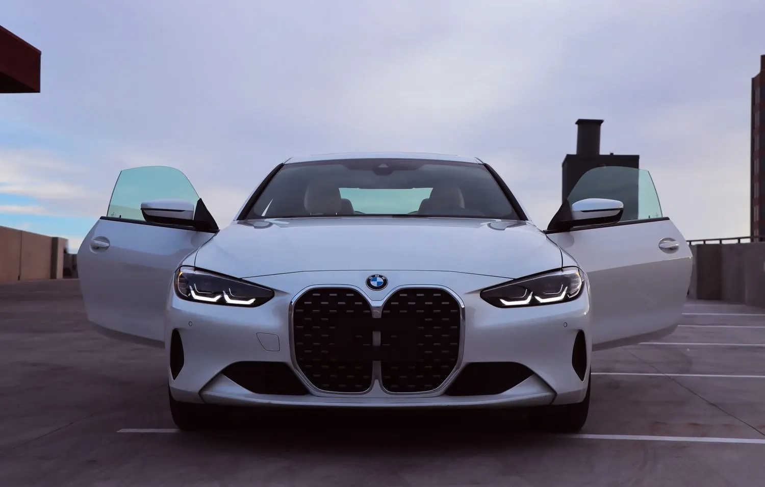A BMW 430i Coupe in Alpine White on the GMS rooftop at Hughes Center, frameless doors open, photographed square-on under an overcast sky
