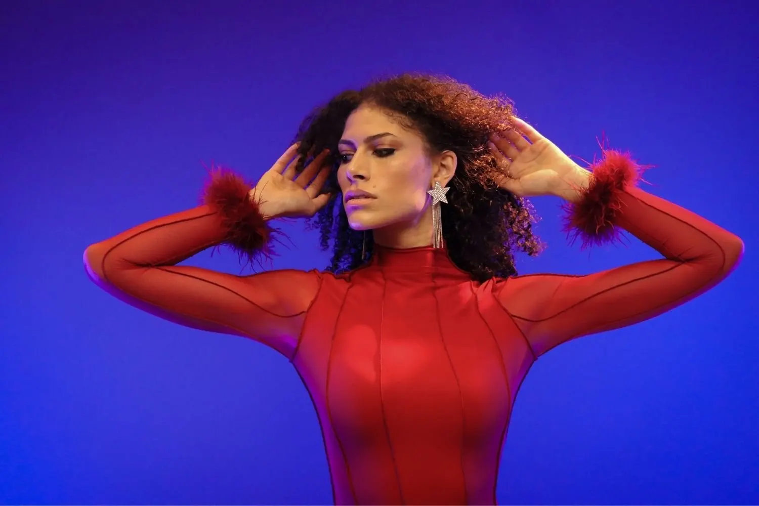 A model in a scarlet feather-cuffed gown against a saturated blue backdrop